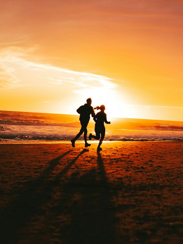Two people running on a beach at sunset